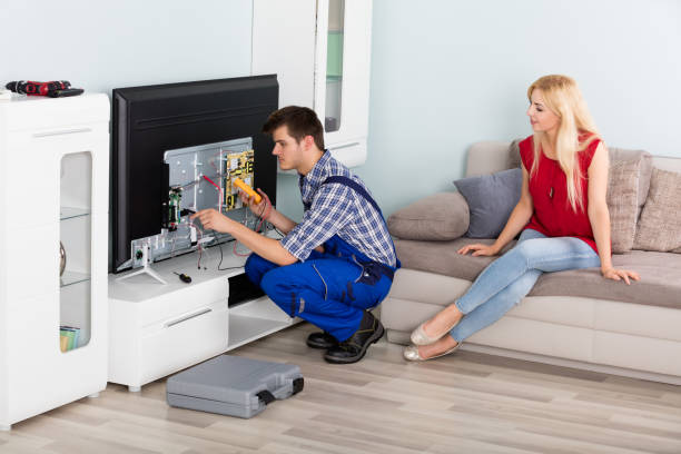 Woman Looking At Technician Repairing Television Young Woman Sitting On Couch Looking At Male Technician Repairing TV At Home installing tv stock pictures, royalty-free photos & images