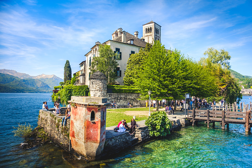 San Giulio island on Lake Orta, Novara province in Piedmont full of tourists relaxing on water edge (Orta Lake, Italy May 21 2017)