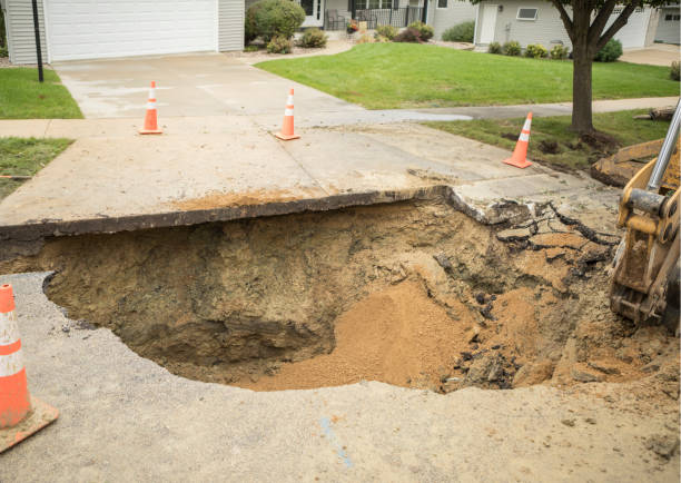 Large Hole in Residential Street from Broken Water Main A large hole in a residential street, near a house driveway, the result of a broken water main. dirt hole stock pictures, royalty-free photos & images