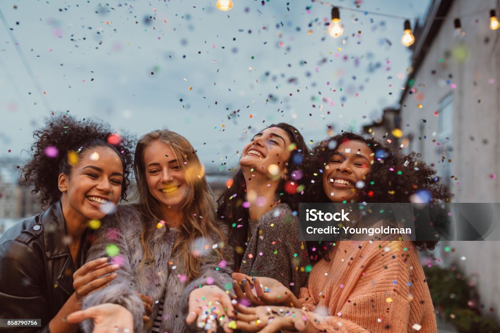 Four beautiful women standing at a terrace under confetti. Women Stock Photo