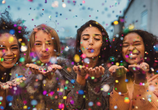 Young women blowing confetti from hands. Young women blowing confetti from hands. Friends celebrating outdoors in evening at a terrace. confetti photos stock pictures, royalty-free photos & images