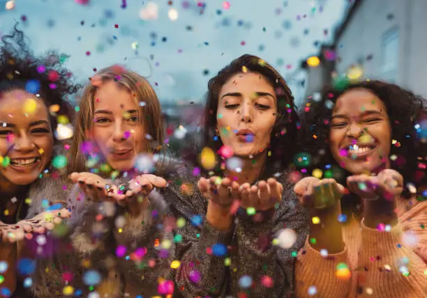 Photo of Young women blowing confetti from hands.