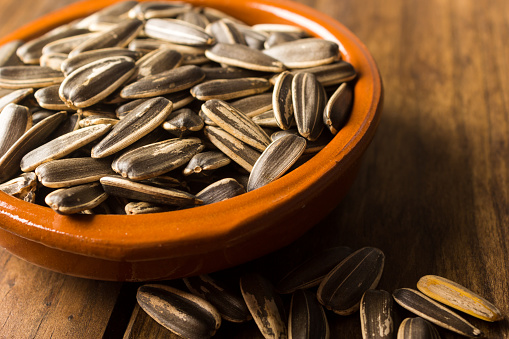 Close up of a group of sunflower seeds in a bowl on a wooden table.