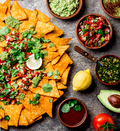 Nachos. Mexican food concept. Yellow corn totopos chips with different sauces salsas - pico del gallo, guacamole, salsa verde, chili pebre and fresh avocado, tomatoes, lemon and cilantro on stone gray background, top view