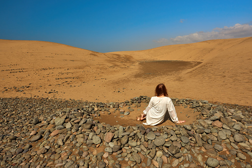 rear view of woman sitting in silence in the middle of the desert, contemplating.photo taken in Maspalomas desert.