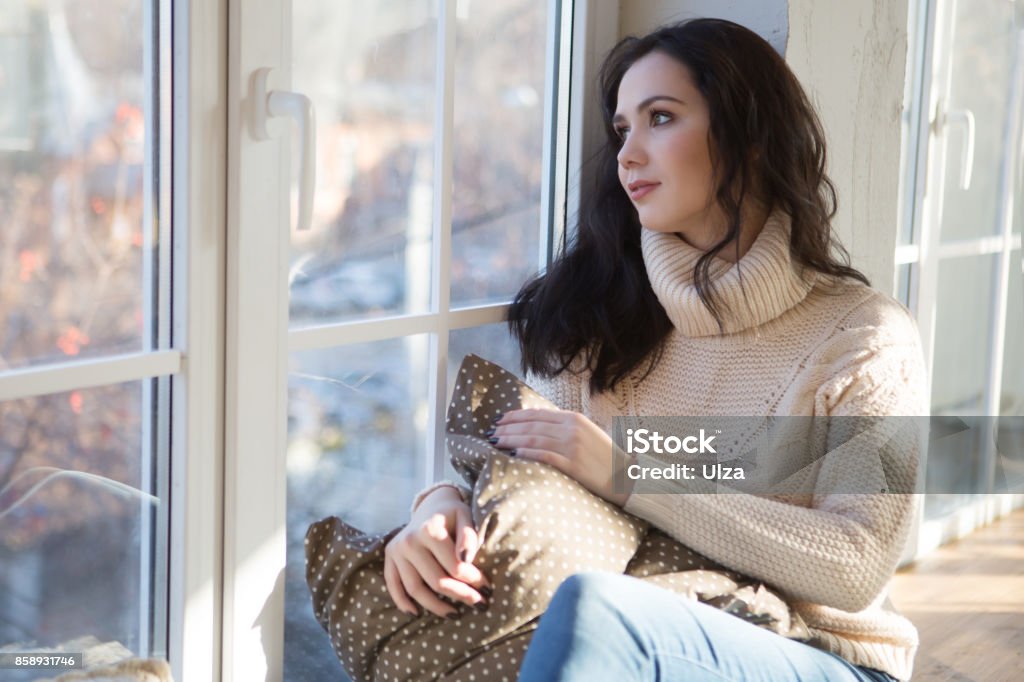 Portrait of Beautiful Young Woman Smiling in a knitted sweater about a window. Christmas morning. Fall Christmas Stock Photo