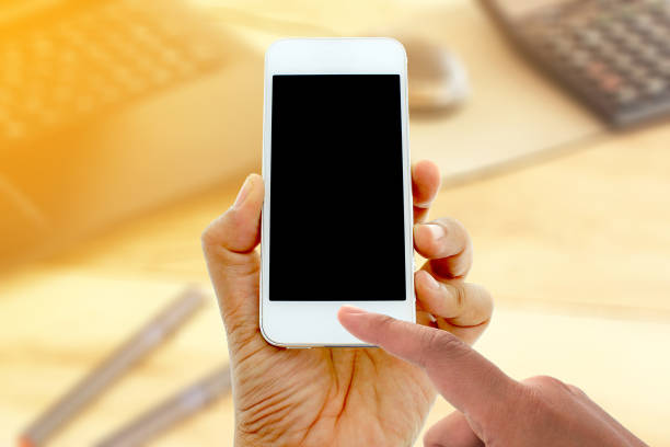 istock hand hold and touch screen smart phone on office desk with laptop computer 858954844