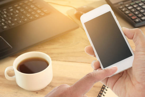 istock hand hold and touch screen smart phone and office desk with laptop computer 858954846
