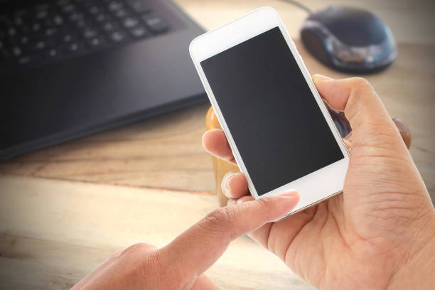 istock hand hold and touch screen smart phone and office desk with laptop computer 858954862