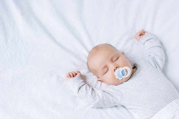 baby with pacifier in mouth sleeping on bed