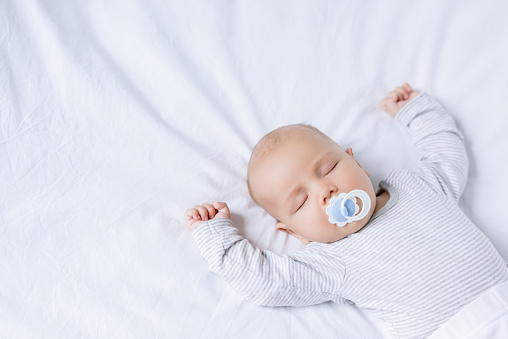 overhead view of baby with pacifier in mouth sleeping on bed