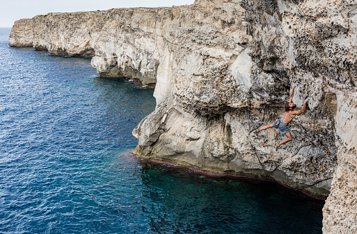 Man practicing deep water soloing rock climbing in Menorca Spain