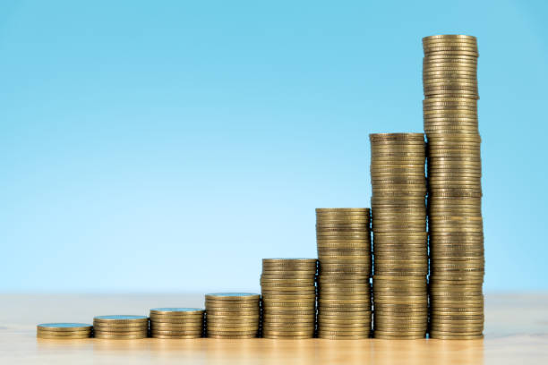 crescente pilha de moedas na mesa de madeira e luz de fundo azul - piggy bank currency savings finance - fotografias e filmes do acervo