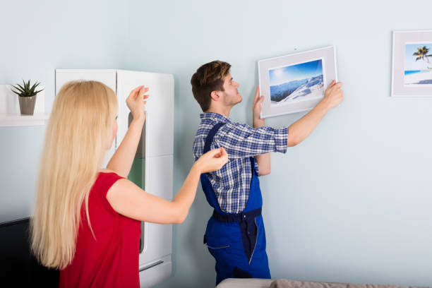 istock Male Carpenter Hanging Picture Frame On Wall 859032722