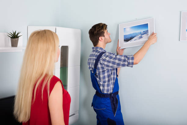 istock Male Carpenter Hanging Picture Frame On Wall 859033328