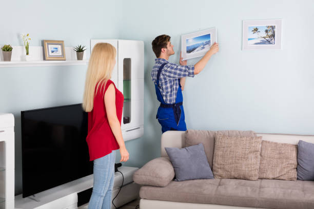 istock Male Carpenter Hanging Picture Frame On Wall 859033512