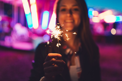 Young woman with burning sparkler outside smiling to the camera