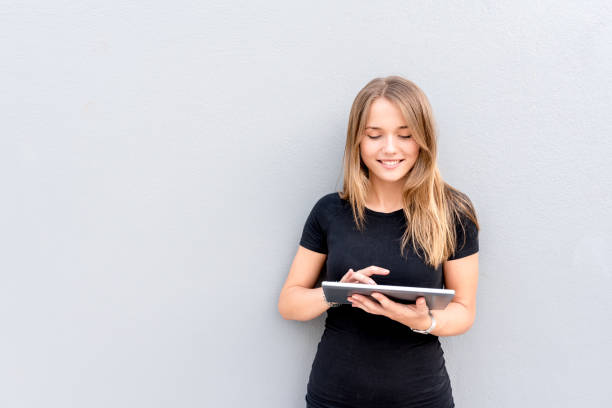 Happy young woman on the tablet by the wall