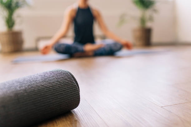 colchonete de yoga no centro de fitness com mulher meditando na parte traseira - estúdio de ioga - fotografias e filmes do acervo