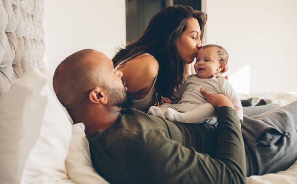 Parents with their newborn baby boy on bed Parents with their newborn baby boy on bed at home. Woman kissing her son sitting with father. young family stock pictures, royalty-free photos & images