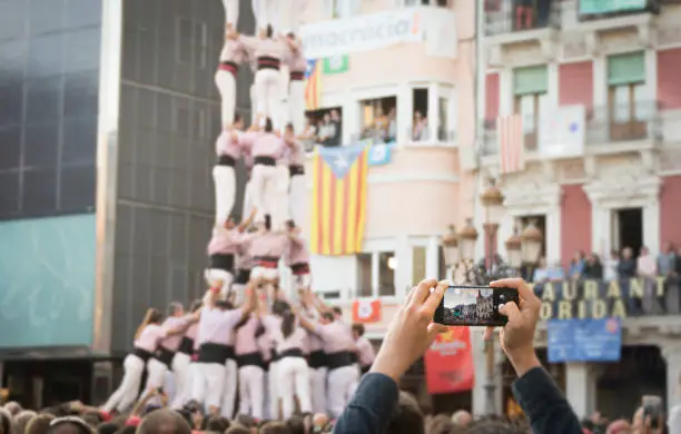 Hand held smartphone taking a picture of Castells Performance. A castell is a human tower built traditionally in festivals within Catalonia. Is also UNESCO Intangible Cultural Heritage of Humanity