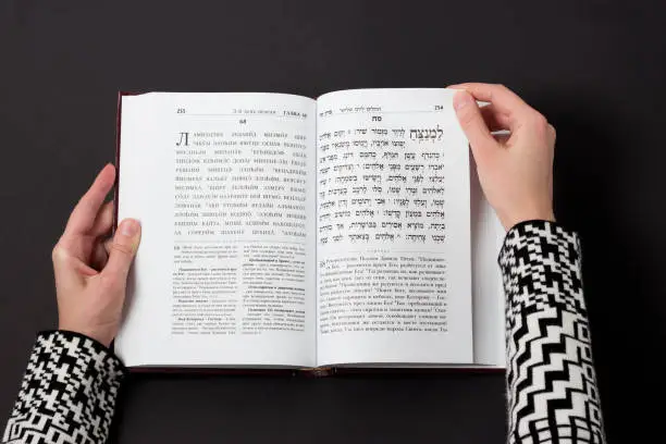 Photo of Jewish book, with woman's hand, on black background. Text of the Hebrew, prayer. Woman reading book.