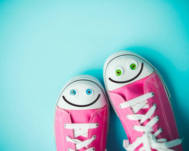 zapatos de lona rosa con caras felices sobre fondo azul - pair fotografías e imágenes de stock