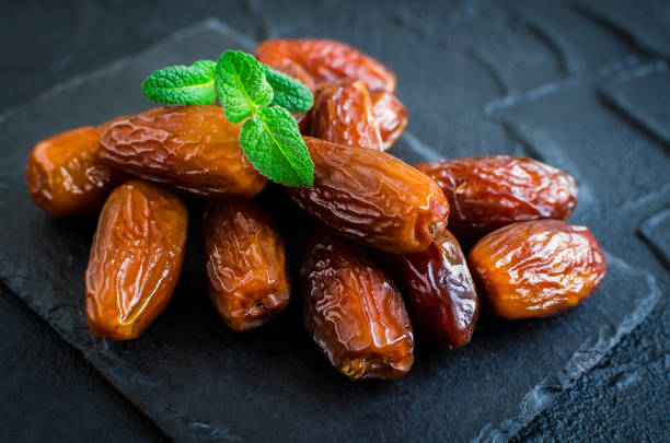 Dried dates on black stone background Dried date and green mint on black stone background. Heap of dates close up. Healthy snack. phoenix stone stock pictures, royalty-free photos & images