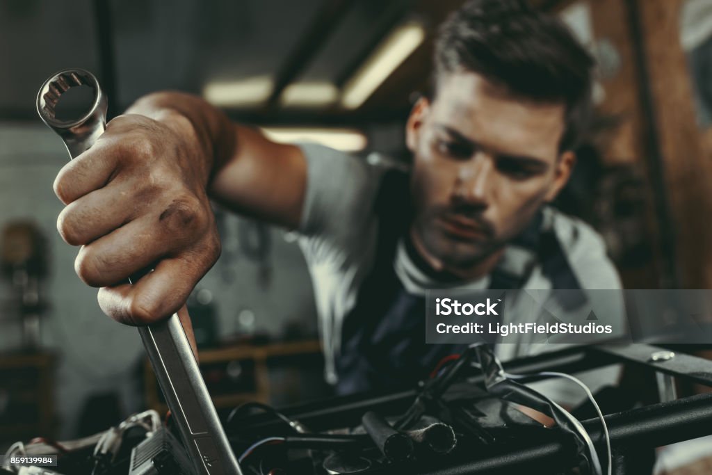 mechanic repairing motorbike young handsome mechanic repairing motorbike in workshop Motorcycle Stock Photo