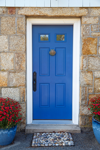 blue door with door knocker, stone doormat and potted plants. Vertical