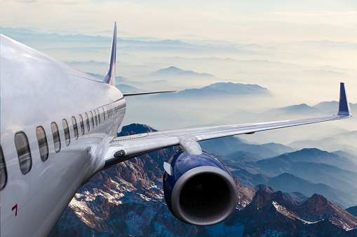 View from the airplane window on the wing to the summer green fields under the clouds. Air transport and travel concept