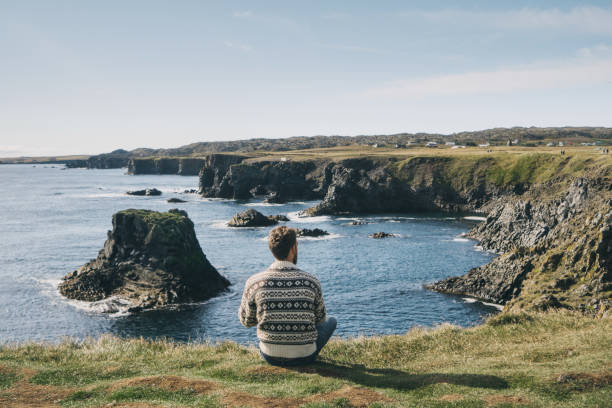 istock Man sitting and looking at the cliffs at seaside  in Iceland 859239980