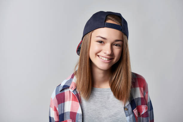 Closeup portrait of smiling teen girl wearing checkered shirt and baseball cap, over grey background