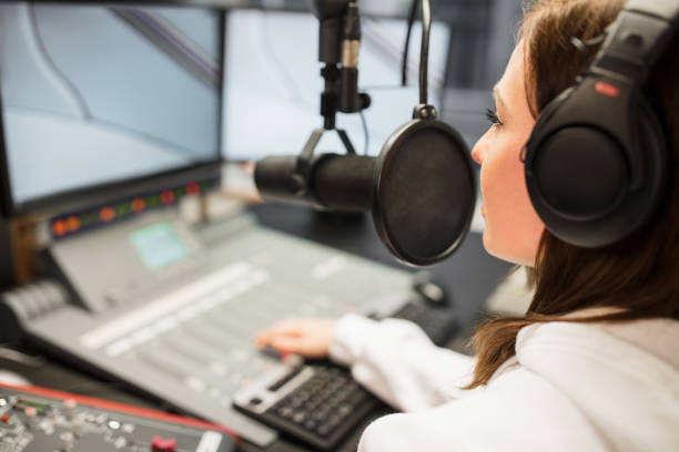 Jockey Wearing Headphones While Using Microphone In Radio Statio Young female jockey wearing headphones while using microphone in radio station radio dj stock pictures, royalty-free photos & images