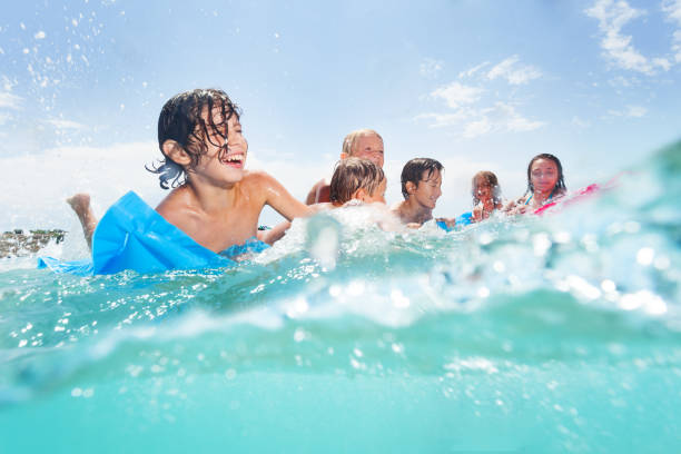 Group of happy kids play in the sea on matrass Group of kids swim and play in the sea water together half underwater image boy laughing with friends matrass stock pictures, royalty-free photos & images