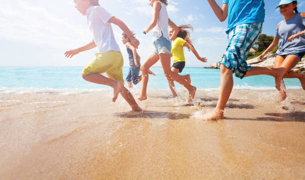 Close-up of running kids legs in shallow sea water Close-up of multiple legs of kids running in shallow sea water with sunlit background wave jumping stock pictures, royalty-free photos & images