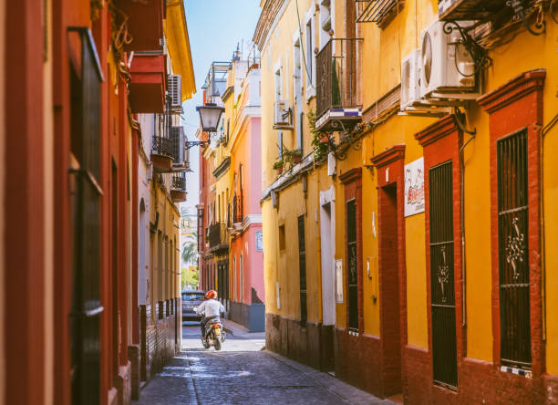 Seville, Spain; September 12th 2017; A spanish man riding a scooter at Triana area in Seville with a bike. Triana area is a traditionla area with colorful buildings and narrow alley.