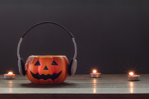 Essential accessory of Happy Halloween decorations festival and music concept background.Mix variety candle items and pumpkin listening radio by headphone on modern rustic wood at home office desk.