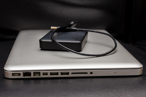 silver laptop with external hard drive on dark black background