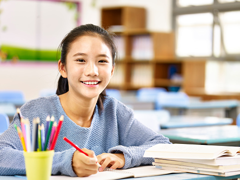 happy asian elementary school student studying in classroom looking at camera smiling,