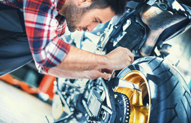 Bike mechanic. Closeup side view of an early 30's car mechanic kneeling next to a racing motorcycle and fixing chain at the rear wheel. bike workshop stock pictures, royalty-free photos & images