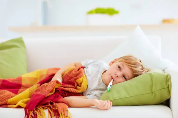 Photo of sick kid with runny nose and fever heat lying on couch at home