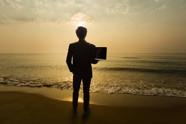 Business Man Standing on the beach in the morning. Are using a notebook computer.