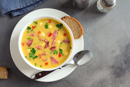 Homemade Corn Chowder Soup with Roasted Ham in white bowl. Healthy creamy corn soup with ham, greens and vegetables.