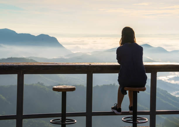 istock Woman sitting on the stool while looking at the panoramic view of mountain range and mist under the sunrise 859335482