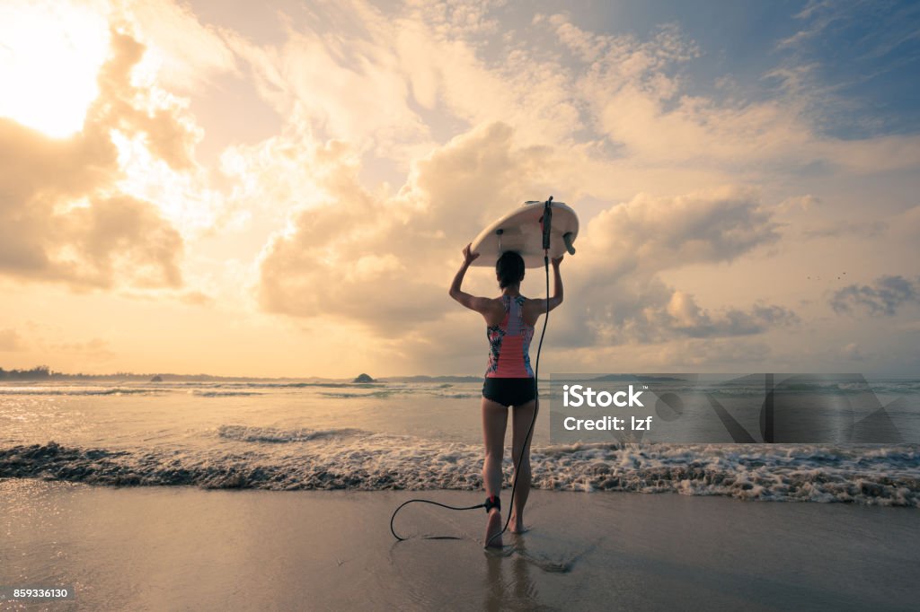 Rear view of young woman surfer with white surfboard walking to the sea One Woman Only Stock Photo