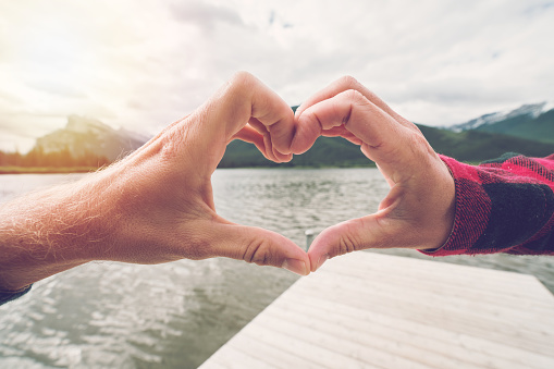 Young couple making a heart shape frame together on mountain lake landscape 