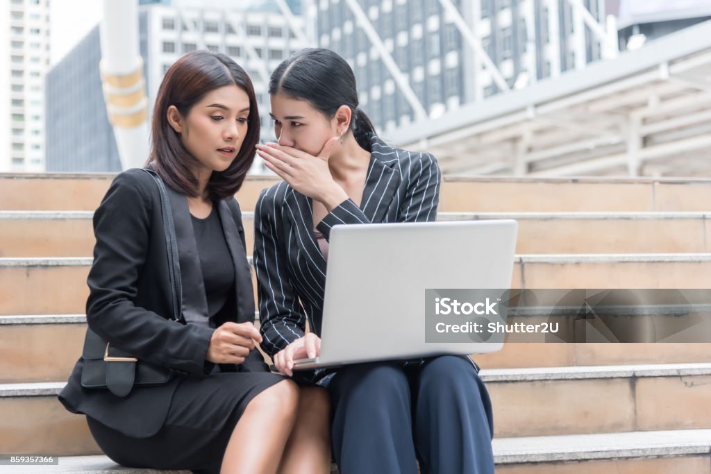 Business women gossip while using laptop at outdoor. Business and coworker concept Whispering Stock Photo