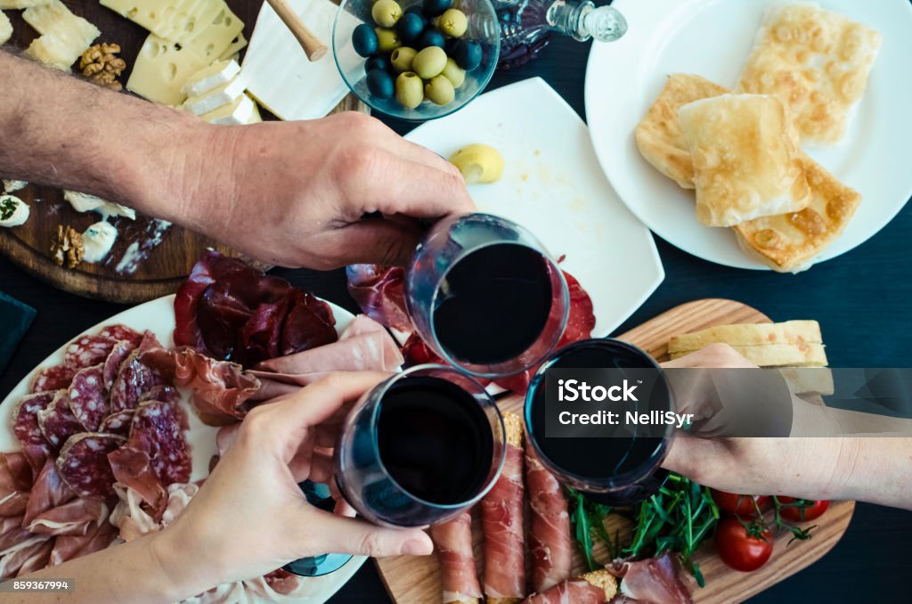 Top view of people toasting with glasses of red wine Top view of people eating and toasting with glasses of red wine. Friends or family different ages enjoying dinner concept. Delicious snack on party or picnic time. Italian style banquet. Wine Stock Photo