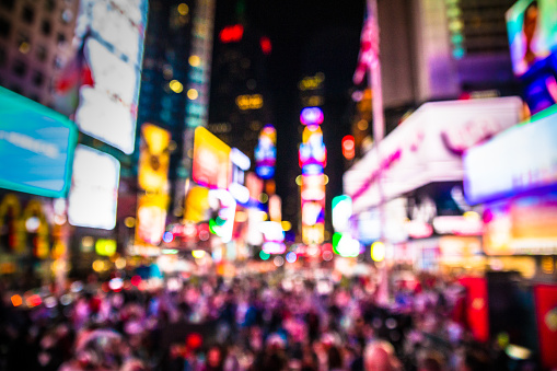 Defocused blur of Times Square in New York City, midtown Manhattan at night with lights and people.